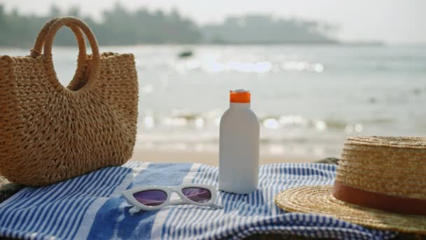 带条纹的毛巾 手提包 太阳镜 防晒霜 用于夏季旅行 光闪闪的大海展现在沙滩上的海滩必需品 — 图库视频影像