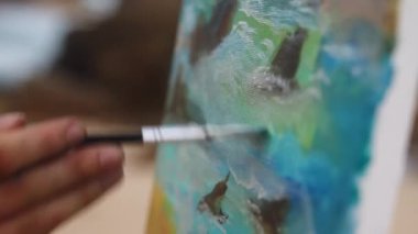 Sanat yaratma süreci, detaylar yakın plan. Ressam kadın tuval üzerinde çalışıyor, fırçayla canlı turkuaz vuruşlar yapıyor. Kadın sanatçının eli, okyanus esinlenilmiş sahneleri, stüdyoda kıyı sanat eserlerini resmediyor. Yavaşla