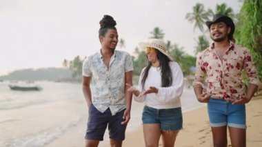 Grup, boş zamanların, çeşitli ve güneşli sahil manzaralarının tadını çıkarıyor. Çeşitli arkadaşlar deniz kenarında geziniyor, şapkalı biri gülüyor, LGBTQ arkadaşlarıyla bağ kuruyor. Sıradan, neşeli sahil gezisi, kapsayıcı atmosfer..