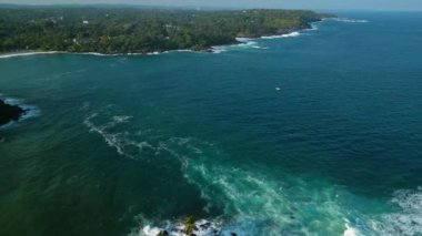 Etrafı yeşilliklerle çevrili tarihi fener etrafındaki kayalıklarda sörf kırılır. Drone Dondra Deniz Feneri, Sri Lanka sahili zeminine karşı. Açık mavi gökyüzü, turkuaz sular, dingin manzara keşfi davet ediyor.