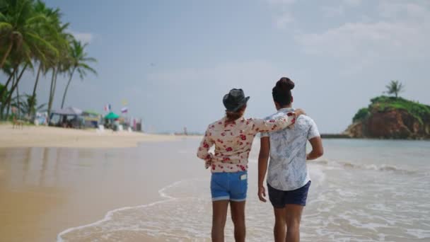 男女同性恋 双性恋和变性者在沙滩上悠闲自在地散步 象征着对多样化关系的包容和自豪 两个男人在海上漫步 手挽手 象征着快乐的爱情 — 图库视频影像