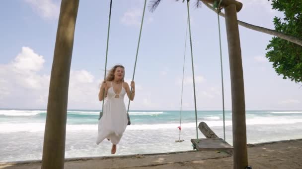 大海的空气 碧水的放松时刻 身穿白衣的女孩喜欢在沙滩上荡秋千 听着海浪声 悠闲的荡秋千之旅 宁静的海滨背景框架体验 — 图库视频影像