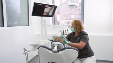 Kadın dişçi, küçük kızların dişlerini intraoral kamerayla inceleyip ekranda izliyor. Doktor dişlerini modern diş kliniğindeki kamerayla kontrol ediyor. Pediatrik dişçilikte intraoral kamera kullanmak.
