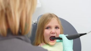 Küçük kız dişçi koltuğunda oturuyor. Modern diş kliniğinde çocukların dişlerini kamerayla inceleyen bir kadın diş hekimi. Pediatrik dişçilikte intraoral kamera kullanmak. İlk diş muayenesi.