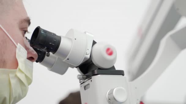 医薬品実験室で顕微鏡を用いた保護フェイスマスクにおける男性科学者の閉鎖 微生物学者はワクチンの実験を行っている 科学者は顕微鏡を用いた研究サンプルを研究する — ストック動画