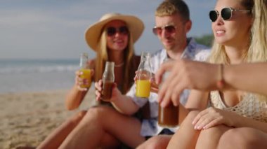 Dört neşeli arkadaş kumlu deniz sahilinde oturur, kombucha içer, tezahürat yapar, tropikal turda sohbet ederler. İki romantik çiftten oluşan kahkaha grubu deniz kıyısında taze meyve suyu şişeleri tokuşturarak rahatlıyor..