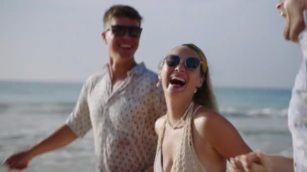 男性の幸せな友人グループ 女性は波に手を飛ばす晴れた熱帯の海浜で走ります 陽気な慎重なカップル 高級リゾートでの旅行休暇で海岸で女性チル — ストック動画