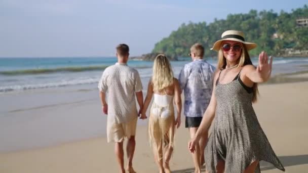 戴着太阳帽的快乐的高加索女人和朋友们轮流走在沙滩上的热带海滩上 请求加入 漂泊在海滨豪华度假胜地的年轻漂亮的女游客兴高采烈地微笑着 请跟来 — 图库视频影像