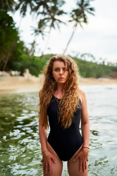 Natural beauty, wellness lifestyle at beachscape. Beautiful woman in swimsuit enjoys sea swim. Female relaxes in tropical water, long hair. Model poses, summer vacation. Ocean, health, tranquility.