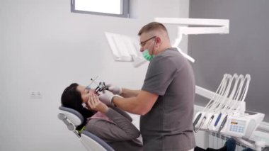 Ortodontist modern diş muayenehanesinde kadın yüzüne diş yayı takıyor. Diş hekimi, hastanın diş hekimliği bilgisi almak için yüz yayı takıyor. Modern kozmetik dişçiliği.
