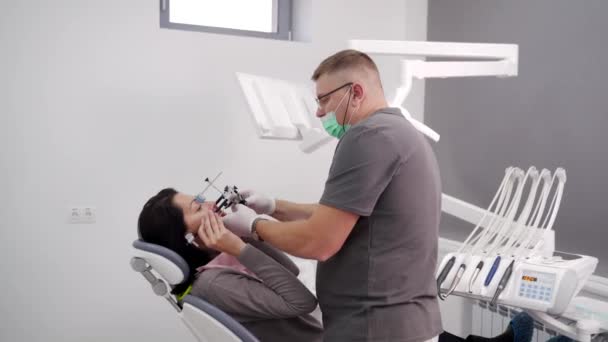 現代の歯科オフィスに女性の顔に歯科の顔を設置するOrthodontist 歯科医は 患者の入れ歯情報を得るために女性患者に顔を設置する 現代化粧品歯科 — ストック動画