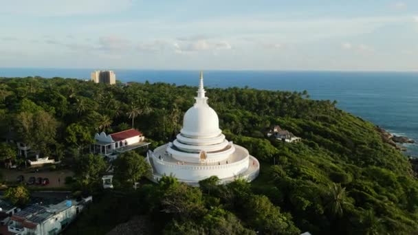 Stupa Buddha Putih Berdiri Melawan Laut Biru Dikelilingi Oleh Pohon — Stok Video