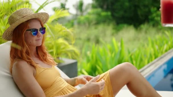 ハンドは新鮮なスイカカクテルを提供しています 太陽の帽子の赤毛の女性 サングラスは熱帯のプールでリラックスします 女性は冷たい飲み物 晴れたレジャーの時間を楽しんでいます 熱い日に爽やかな飲み物 冷たい休暇のバイブ — ストック動画