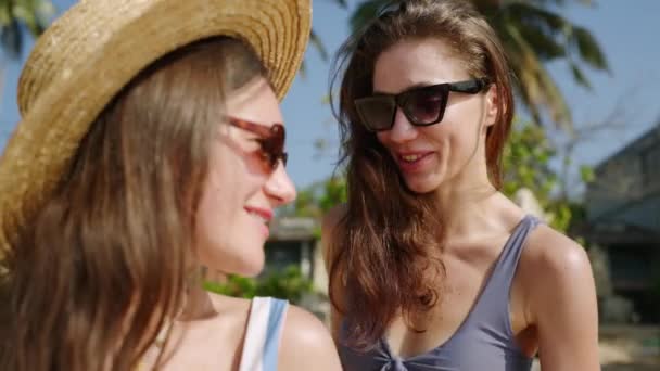 幸せな若い女性は友人が熱帯のビーチでサンクリームを塗るのを助けます 陽気な女の子は 楽園の島 ヤシの木で日焼けする 女性の友人がローションを使用しています クローズアップ — ストック動画