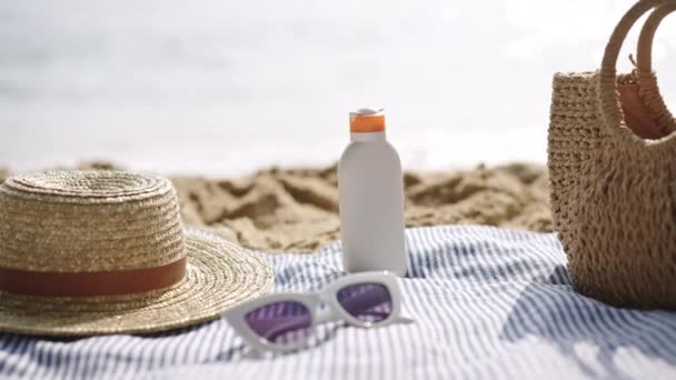 日焼け止めボトル 紫外線保護 ウィッカーの付属品とともに 青いストライプタオルに配置されたビーチの必需品 オーシャンフロントのシーンは 夏のレジャー スキンケアの必要性 休暇の雰囲気を描いています スローモーション — ストック動画