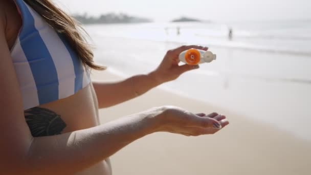 ボトルからサンクリームを絞り 海辺で手で塗る女性の手 ビキニの若い女性は ビーチで肌に防水日焼け止めをかけています Spfを適用する女の子 スキンケアのコンセプト クローズアップ — ストック動画