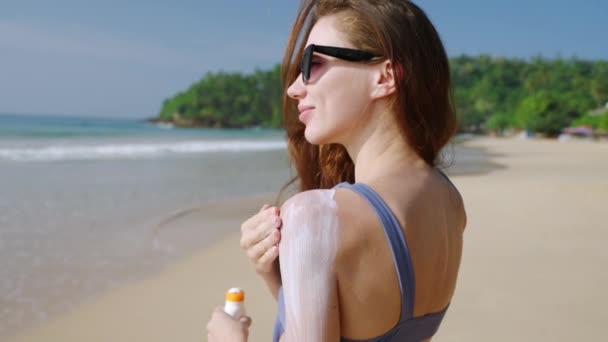 かなり慎重な少女は日焼け止めを防水する日焼け止めを夏の晴れた日に海に置きます 女性は熱帯のビーチで安全な日焼けのために皮膚に耐水性のスプーフを適用します 夏のスキンケアルーチン — ストック動画