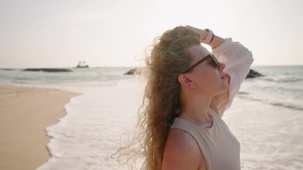 선글라스에 매력적인 파도에서 머리를 만지는 여자는 해변에서 바람에 해안에서 클로즈업 — 비디오