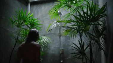 Tropikal bir ortamda rahatlarken su onun üzerine dökülüyor, sağlığını ve huzurunu somutlaştırıyor. Çok ırklı kadınlar yemyeşil havayla çevrili açık hava duşlarını severler. Yavaş çekim.