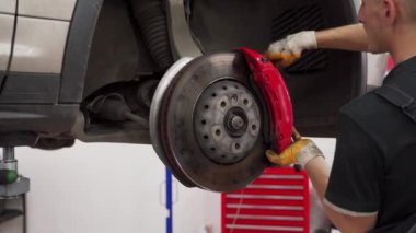 Profesyonel garajdaki fren yastıklarını değiştiriyor. Otomatik tamirci arabaya yeni disk freni takıyor. Araç bakım işi, eldiven takmak frenleri tamir etmek, kalibreli tesisat, oto tamir servisi..