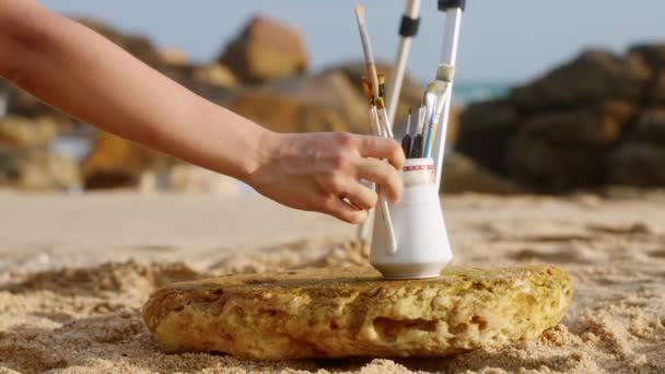 帆布站在岸上 调色板 油画准备好艺术创造 艺术女人在阳光灿烂的海滩上准备绘画工具 背景中的岩石激发了创造力 画家开始了 — 图库视频影像