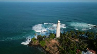 Büyük dalgalar körfeze çarpar, palmiye ağaçları sallanır. Drone görüntüleri tropikal sahildeki görkemli klasik deniz fenerini gösteriyor. Tarihsel deniz feneri denizcilere yol gösteriyor, masmavi okyanusa bakıyor, kumlu plaja bakıyor..