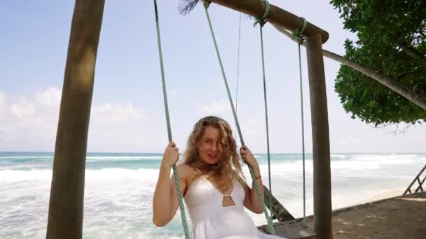 Zorgeloze Vrouwelijke Schommels Haarstromen Oceaanachtergrond Meisje Witte Jurk Geniet Van — Stockvideo