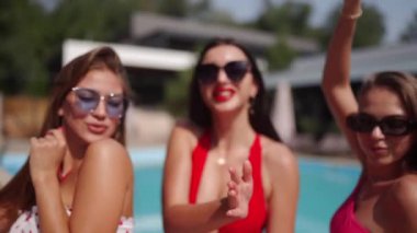 Parlak renkli bikinili ve güneş gözlüklü kadınlar lüks kulüpte şişme daireyle havuz turkuaz suyunda poz veriyorlar. Arkadaşlarla yaz partisi, eğlence, müzik, kahkaha, flört, dans.