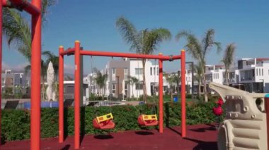 Modern villaları, yeşil peyzajı, güneşli havası, varlıklı açık hava aktivitesi olan lüks konut kompleks oyun sahasında boş çocuklar sallanıyor..
