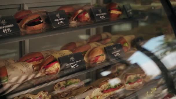カフェ 新鮮な 包まれた 販売のためのラベル付き おいしいディスプレイケースのグルメサンドイッチ 多様なランチオプション クローズアップ 人なしを提供するカフェ — ストック動画