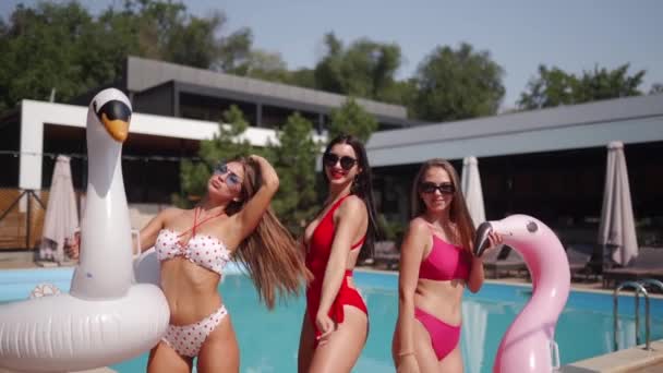 身穿鲜艳色彩艳丽的比基尼和太阳镜的女模特们在豪华俱乐部的游泳池边摆出碧绿的水和充气圆圈 与朋友的夏季派对 — 图库视频影像