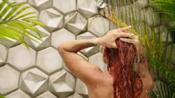 她在流水里摸着她的头发 周围是茂密的植物 几何图形的瓷砖设计增强了宁静的氛围 红头发的女人在奢华的热带环境中享受新鲜的户外淋浴 — 图库视频影像