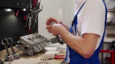 Profesyonel mekanik motor kitini birleştirir, piston halkalarını odaklı ve hassas bir şekilde silindir çizgisine yerleştirir, araçlar ve bileşenler ile çalışma tezgahı görünür, ilerleyen motor bakımında otomatik onarım.