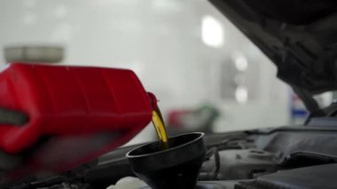 Performans optimizasyonu için filtreli araç bakımı, sıvı kontrolü, otomatik servis. Oto teknisyeni motor yağını değiştiriyor, araba bakım garajındaki huniden taze yağ döküyor..