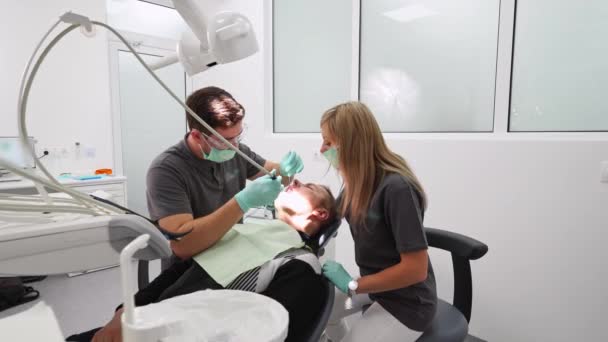 在现代牙科诊所治疗牙齿 牙科医生和助手治疗病人龋 护士和病人在牙科诊所 团队合作期间的口腔外科医生和助理 — 图库视频影像