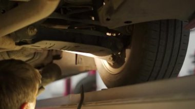 Güvenlik ve bakım için otomotiv sistemlerinin profesyonel denetimi. Otomobil tamircisi araba süspansiyonunu kontrol etmek için hidrolik oyun detektörü kullanır, servis bölümünde aracın altında direksiyon sallar.