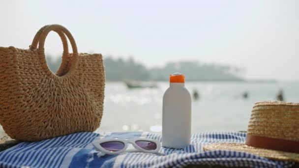 サマースキンケア レジャー スパークリングオーシャンによるバケーションアクセサリー 晴れた季節の日のビーチの必需品 トレンディなわら帽子 バッグ タオルのサングラスと一緒に日焼け止めSpfとボトル — ストック動画
