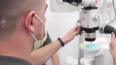 Modern dişçilik kliniğinde diş mikroskobuyla çalışan erkek dişçi. Cerrah mikroskop kullanarak cerrahi operasyon gerçekleştirir. Kozmetik dişçiliği ve ameliyat. Stomatoloji ofisinde tıbbi prosedür.