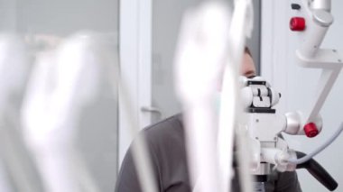 Erkek dişçi modern diş hekimliğinde mikroskop kullanarak hastayı tedavi ediyor. Doktor mikroskopla çalışır, kaplamaları yerleştirir. Ağız cerrahı, kanal tedavisi. Modern diş ekipmanları.