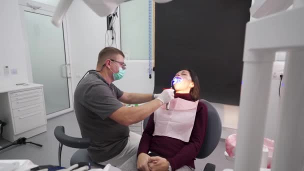 牙科医生在牙科诊所用紫外光灯把妇女的牙龈 牙冠粘合在一起 氧化锆饰品的安装过程 牙科医生用紫外光激活胶水以安装牙冠 — 图库视频影像