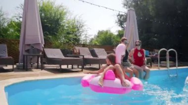 Modeller şişme borularla dans eder, arkadaşlar mavi havuza atlayıp eğlenirler. Bir grup kadın ve erkek, sıcak güneşli bir günde, gece kulübünde dinleniyor..