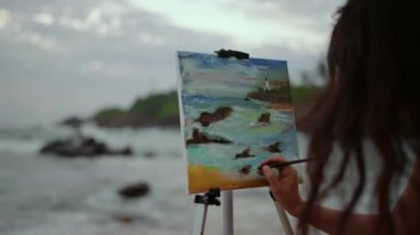 Sanata odaklanmış, renkleri harmanlıyor, okyanus güzelliğini, dalgaları, günbatımını yakalıyor. Dişi ressam plajda canlı deniz manzarası çizer, alacakaranlık ışığı renkleri yükseltir. Yaratıcı an, sahil şeridi ilhamı.