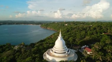 Beyaz Budist salağı tepede duruyor, mavi okyanusa bakan yeşil yapraklarla çevrili. Unawatuna 'daki Japon Barış Pagoda' sı üzerinde hava manzarası. Sri Lanka kıyısında kutsal mimari.