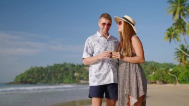 Romantik çift, tropikal seyahatte bir kadın güneşli sahil sahilinde elinde limonata şişeleriyle kameraya bakar, klink, chat, kahkaha. Neşeli beyaz erkek, randevuda dişi deniz kıyısında içkinin tadını çıkar..