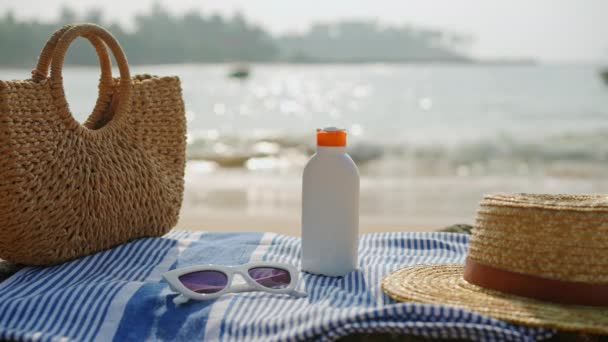 防晒霜瓶 太阳镜 柳条袋 用于护肤 海滨必需品摆放在海边的条纹毛巾上 利用紫外线护理产品在海上度假 — 图库视频影像