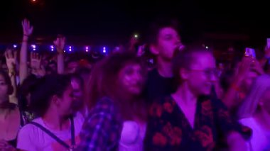 2021-08-07 - Mariupol Şehir Festivali, Ukrayna. Heyecanlı hayranlar dans ediyor, renkli sahne ışıkları altında el kaldırıyor. Gece müzik festivalindeki kalabalık canlı performansın keyfini çıkarıyor. Akıllı telefonları olan izleyiciler.
