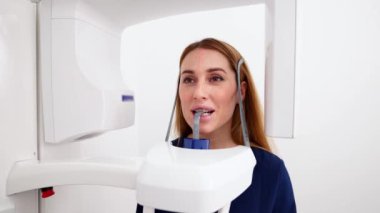 Panoramik röntgen çekiminde, yüzü röntgen makinesinde tutan bir kadın hasta. Diş röntgeni ünitesindeki kadın diş röntgeni için lazer projeksiyonu yapıyor. Modern bir klinikte dişleri inceliyorum..