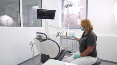 Kadın dişçi, modern diş muayenehanesindeki küçük bir hastayla sandalyeyi ayarlıyor. Kadın stomatolog küçük kızların dişlerini klinikte muayene ediyor. İlk diş muayenesi. Pediatrik dişçilik.