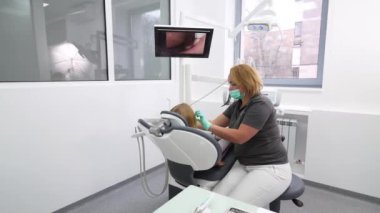 Kadın dişçi, küçük kızların dişlerini intraoral kamerayla inceleyip ekranda izliyor. Doktor dişlerini modern diş kliniğindeki kamerayla kontrol ediyor. Pediatrik dişçilikte intraoral kamera kullanmak.