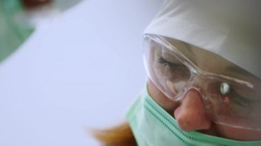 Gözlüklü kadın ağız cerrahı, implant ameliyatı sırasında yüz maskesi. Modern diş kliniğinde ameliyat sırasında cerraha yardım eden hemşire. Konsantre dişçi diş implantı yerleştiriyor. Yakın plan..